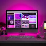 Modern desk setup with neon lighting and a desktop computer displaying colorful images.