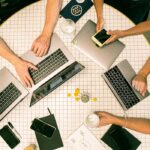 Top view of a team collaborating with laptops, phones, and notes in a modern office.