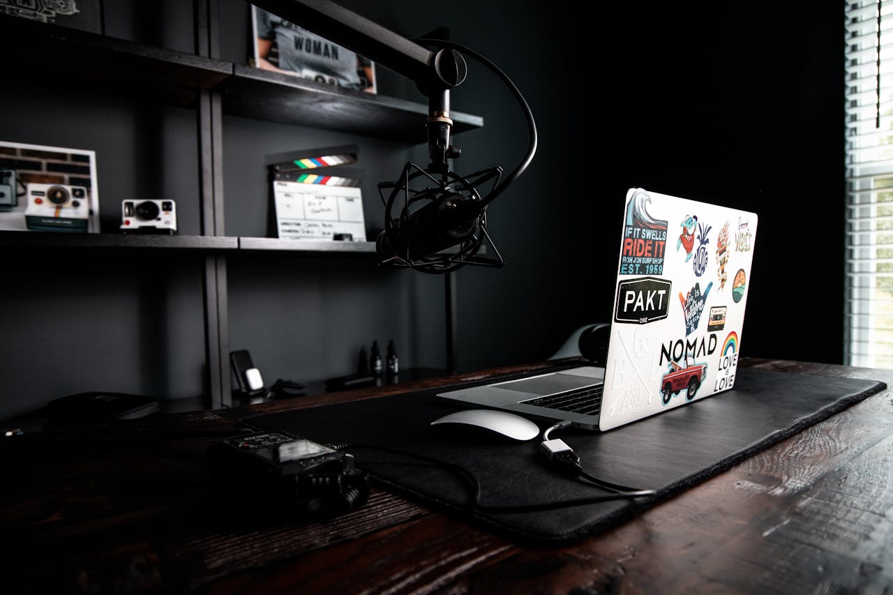 Creative workspace featuring a laptop, microphone, and clapperboard on a wooden desk, ideal for podcasting.