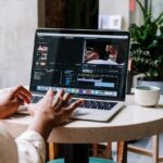 Freelance video editor working on a laptop in a cafe setting, utilizing Adobe software.